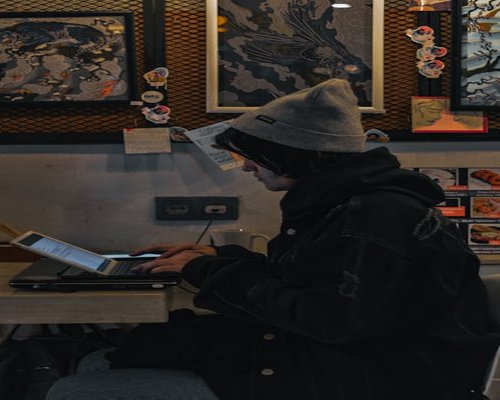 Person adjusting sitting posture while working on a laptop at a cafe in Bandung